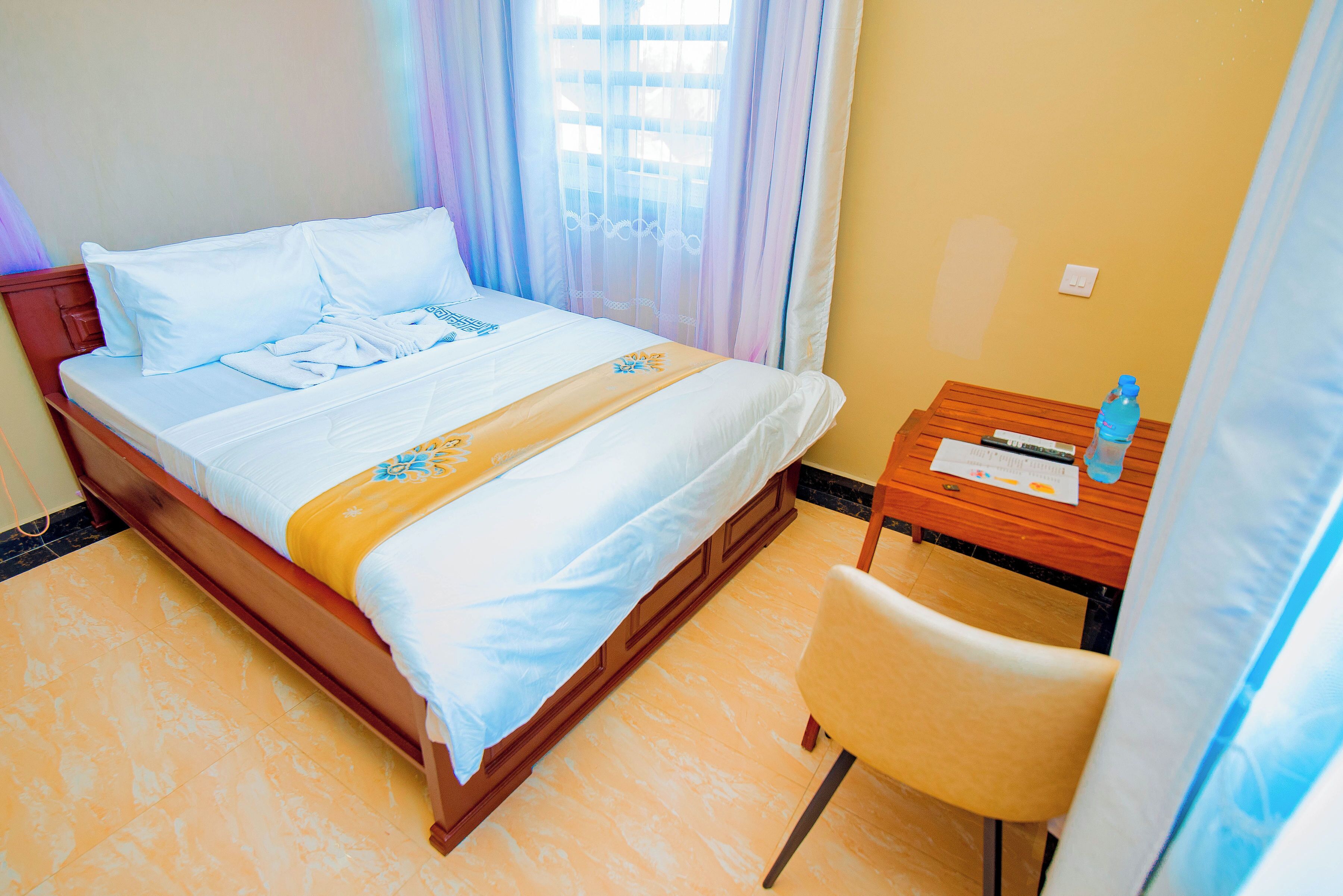A hotel room with a bed, a wooden nightstand, a chair, and a window with curtains.