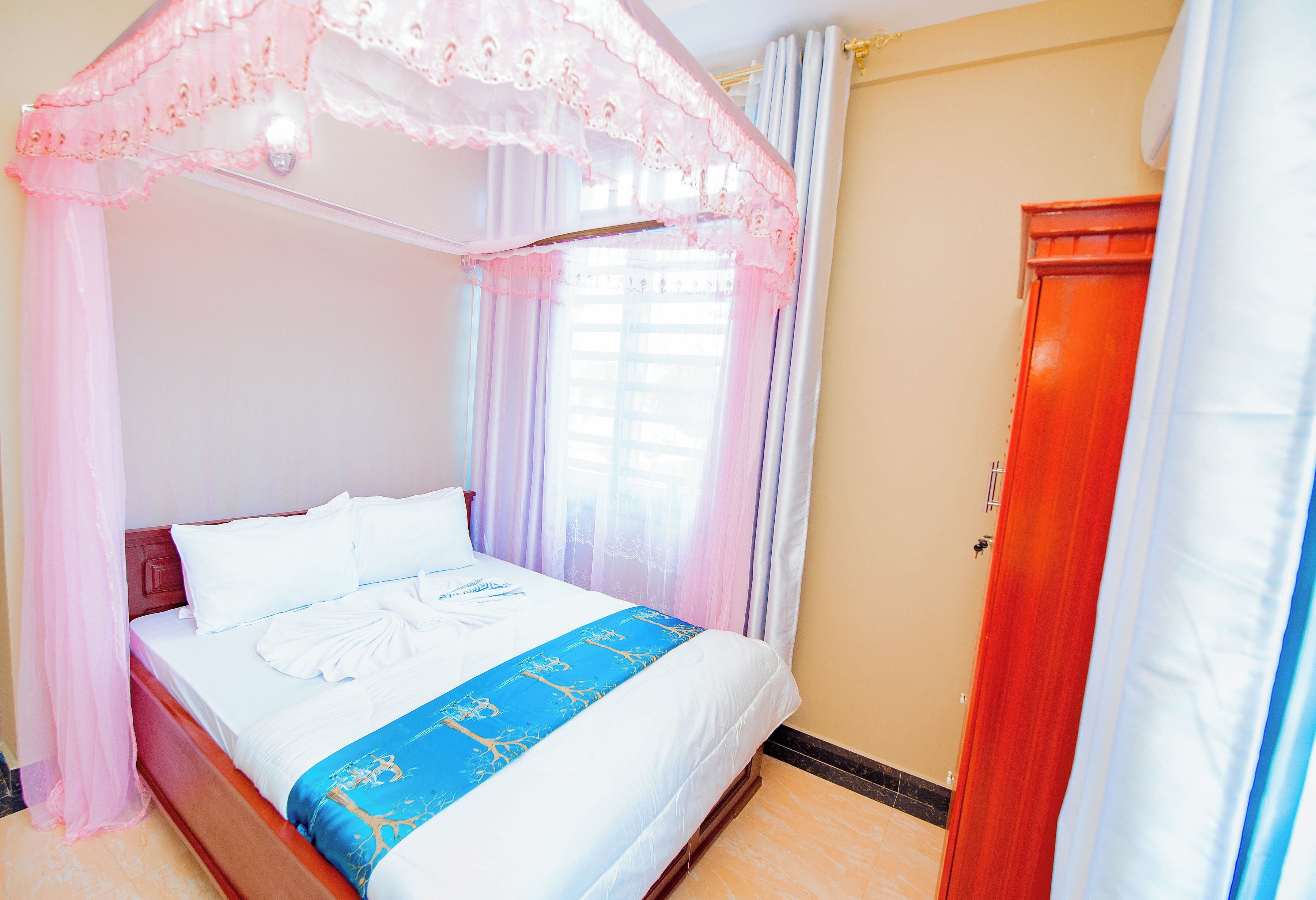 A neatly made bed with a blue and white bedspread, a wooden headboard, and a canopy with lace detailing.