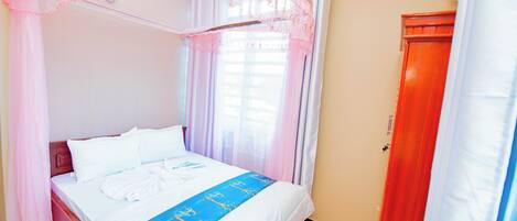 A neatly made bed with a blue and white bedspread, a wooden headboard, and a canopy with lace detailing.