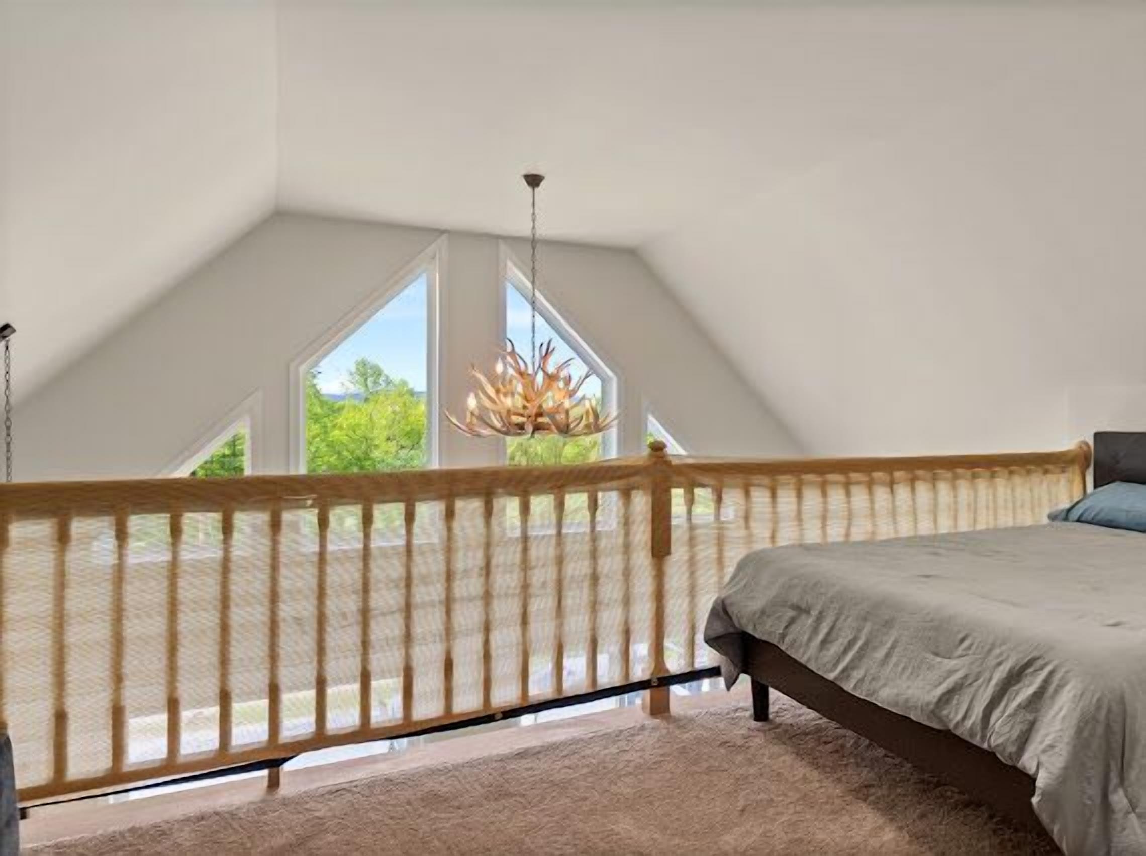 Une chambre avec un plafond en pente, un lit, un luminaire suspendu et une vue sur la verdure à l’extérieur.