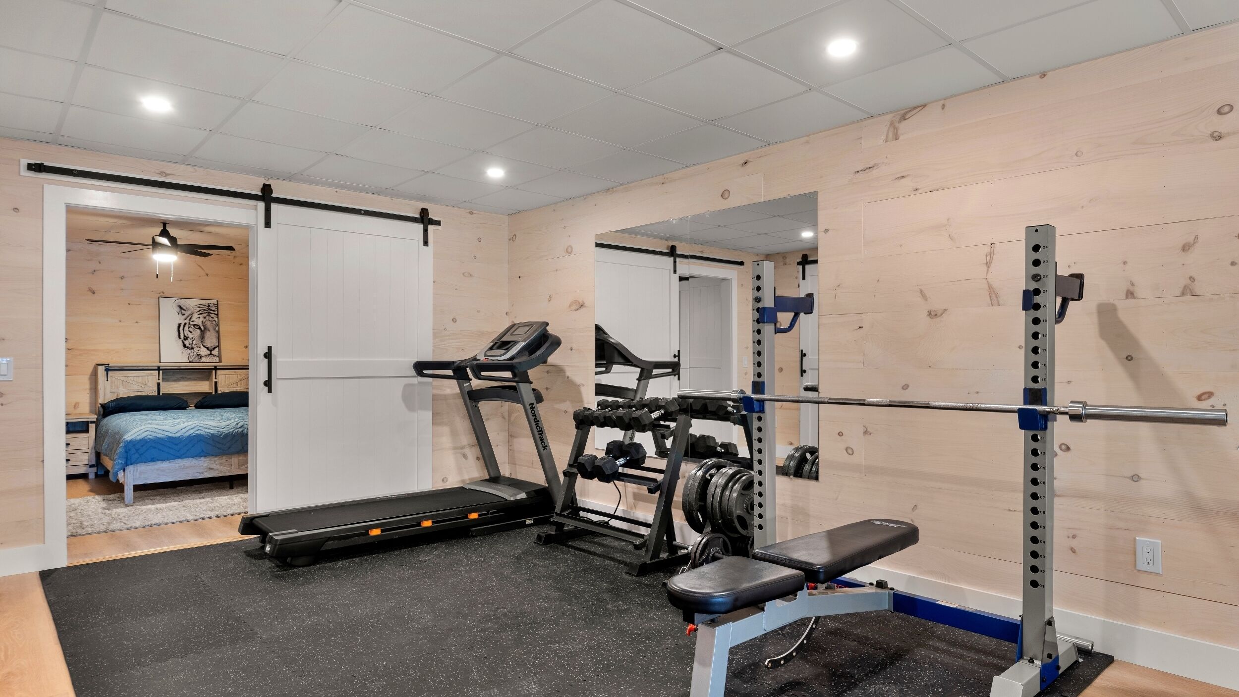 Een sportschool met een loopband, een gewichtbank en een squats rek.
