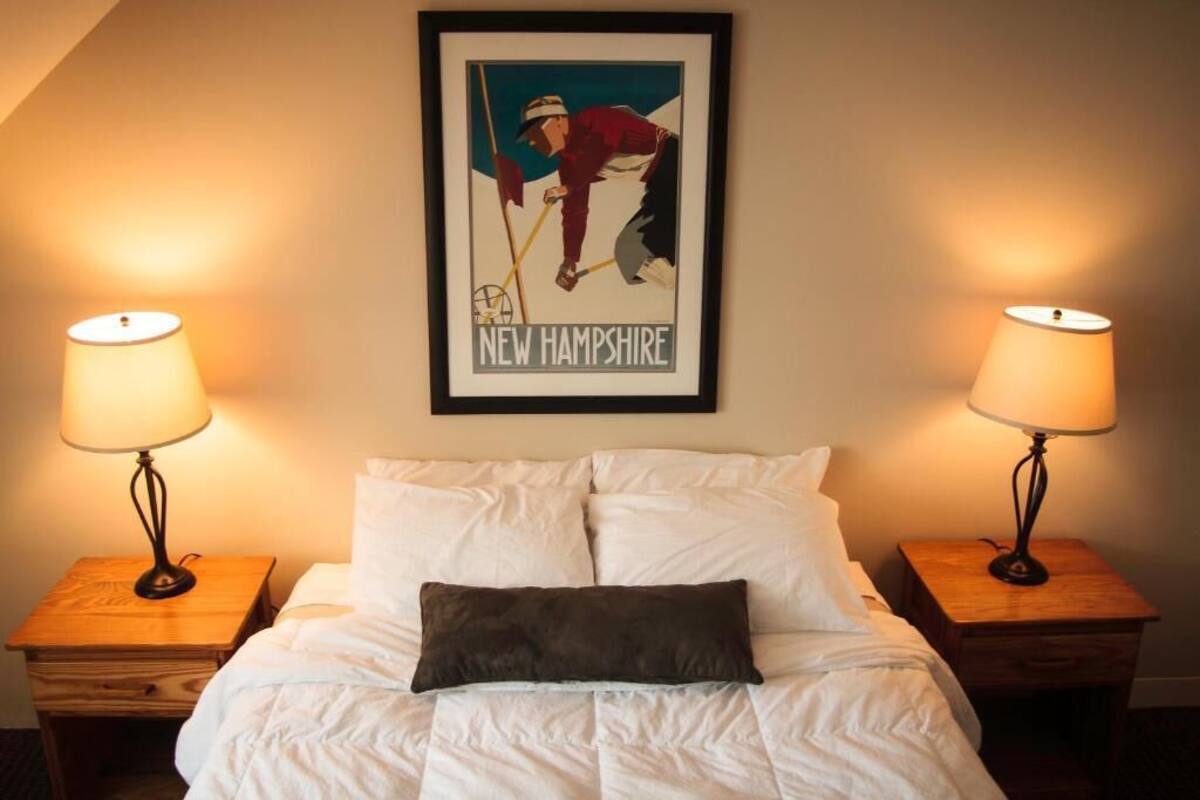 Ein ordentlich bezogenes Bett mit weißer Bettwäsche und einem dunklen Kissen, flankiert von zwei Nachttischen mit Lampen, und ein gerahmtes Poster eines Golfers an der Wand darüber.