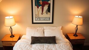 A neatly made bed with white bedding and a single dark pillow, flanked by two wooden nightstands with lamps, and a framed poster of a golfer on the wall above.