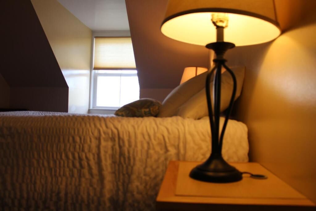 Un dormitorio con cama, lámpara y ventana.