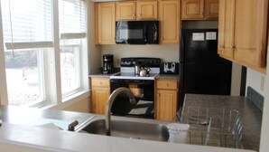 A kitchen with wooden cabinets, a black microwave, a stove, and a refrigerator.