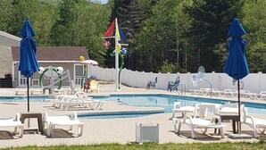 A pool area with lounge chairs and umbrellas, surrounded by trees and a building.
