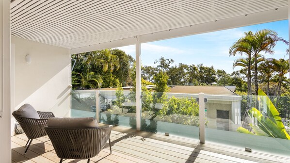 Un balcon doté d’une balustrade en verre, d’un fauteuil confortable et offrant une vue sur les arbres et les bâtiments.