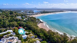 Vue aérienne d’une zone côtière comprenant une plage, des immeubles résidentiels et un paysage montagneux en arrière-plan.