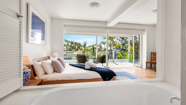 Un dormitorio moderno con una cama grande, vistas a un jardín tropical y un ventanal corredero que da a un espacio al aire libre.