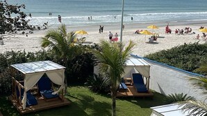 A beach with tents and umbrellas, a grassy area, and a view of the sea. - Ingleses Praia Hotel (Florianópolis)