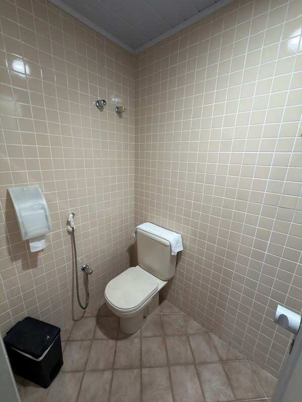 A small bathroom with a toilet, a hand dryer, and a shower head.