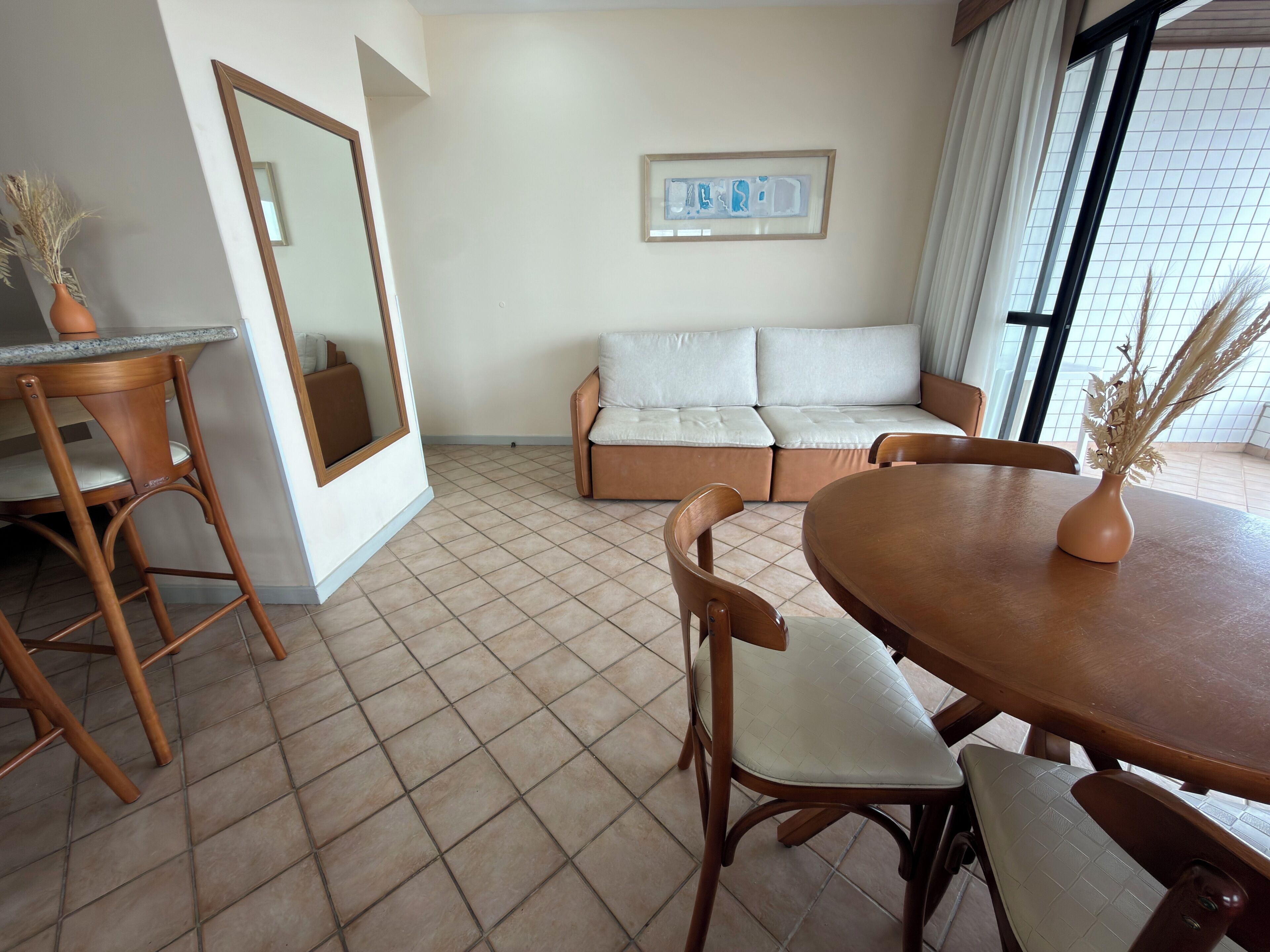 A room with a dining table, chairs, a sofa, a mirror, and a framed picture on the wall.