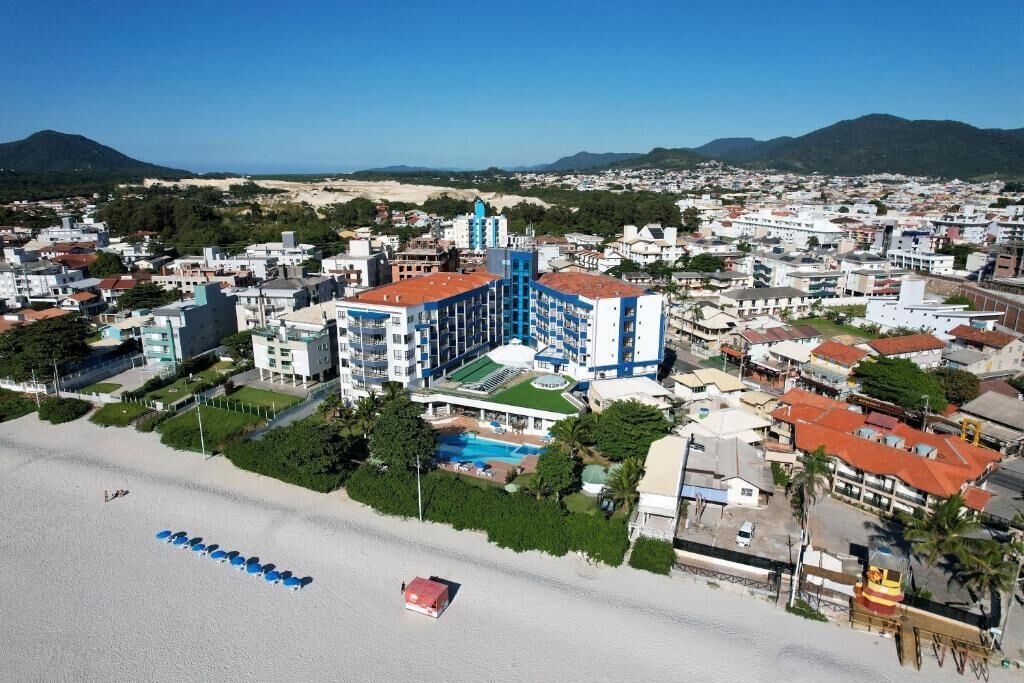 A coastal hotel with multiple buildings, a beach, and a mountain in the background.