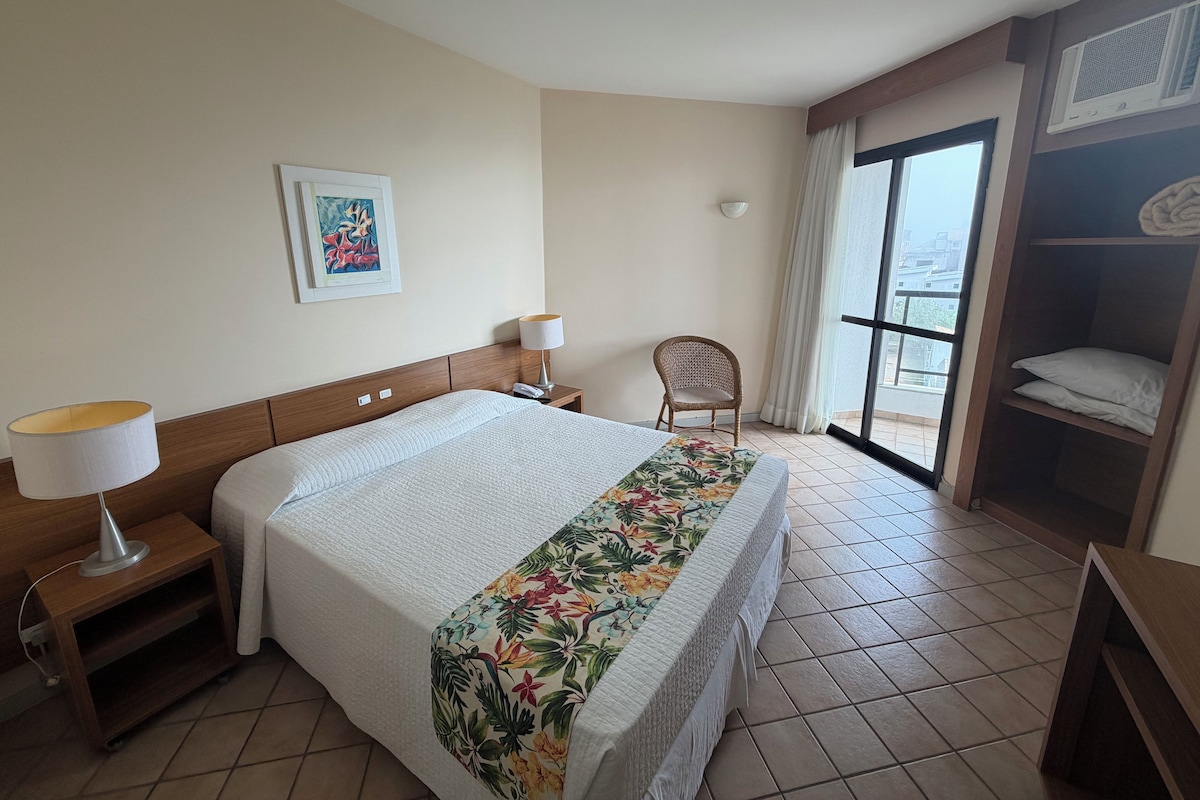 A hotel room with a bed, two bedside lamps, a chair, a window, and a wardrobe.