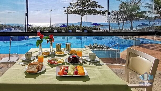 A breakfast table with a view of a swimming pool and beach. - Ingleses Praia Hotel (Florianópolis)