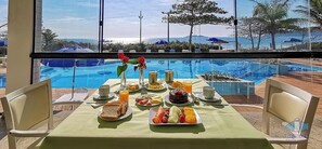 A breakfast table with a view of a swimming pool and beach.