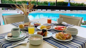 A breakfast table with various dishes and drinks, overlooking a swimming pool. - Ingleses Praia Hotel (Florianópolis)