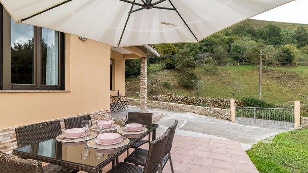 Eine Terrassensitzgruppe im Freien mit Tisch für vier Personen, umgeben von Korbstühlen, unter einem großen Sonnenschirm.