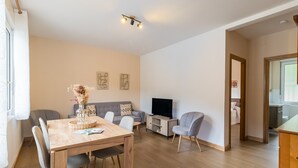 Ein modernes Wohnzimmer mit Esstisch aus Holz, grauen Sofas, einem Fernseher und einer Küchenzeile.
