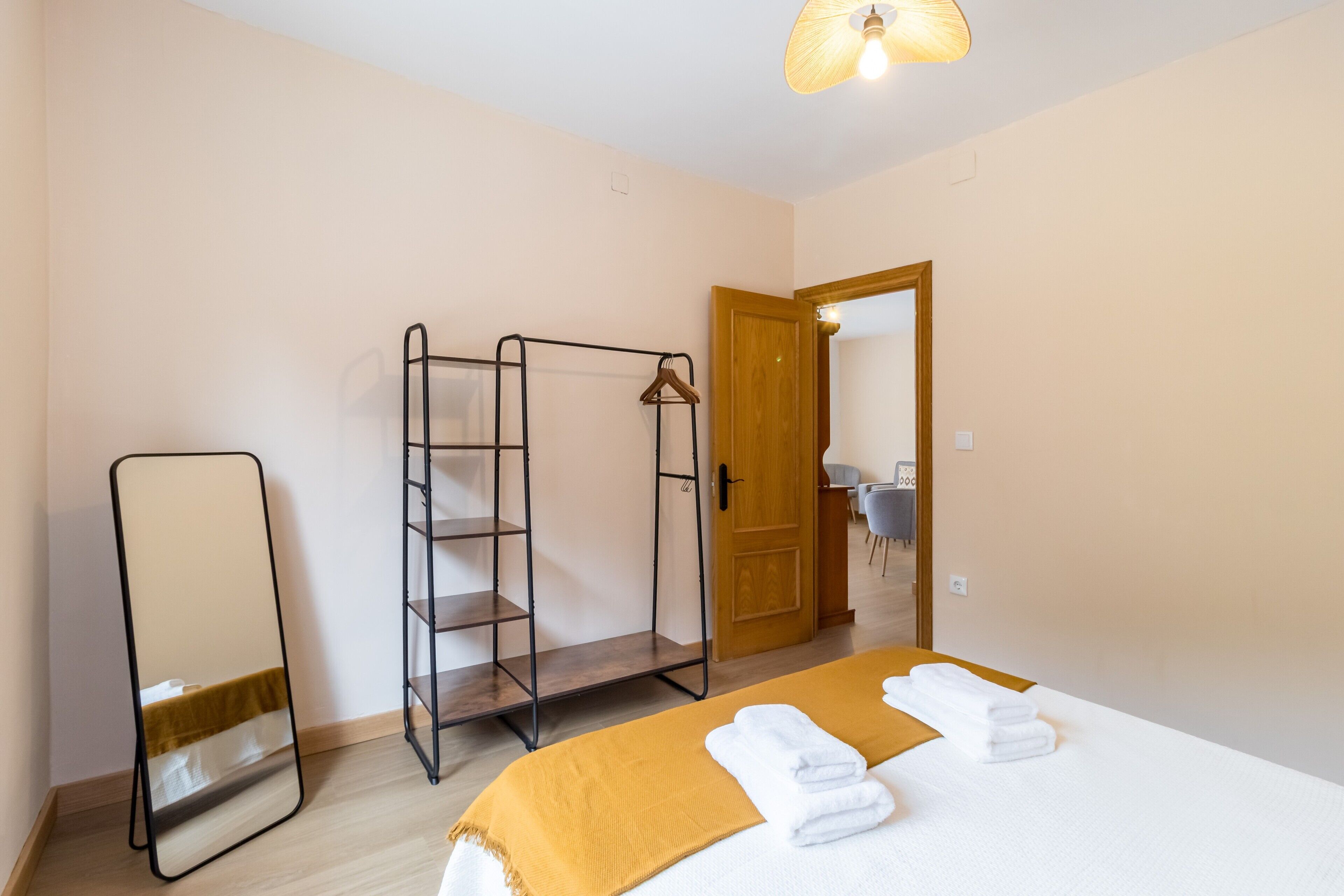 A bedroom with a bed, a wooden door, a mirror, and a metal shelf unit.