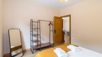 A bedroom with a bed, a wooden door, a mirror, and a metal shelf unit.