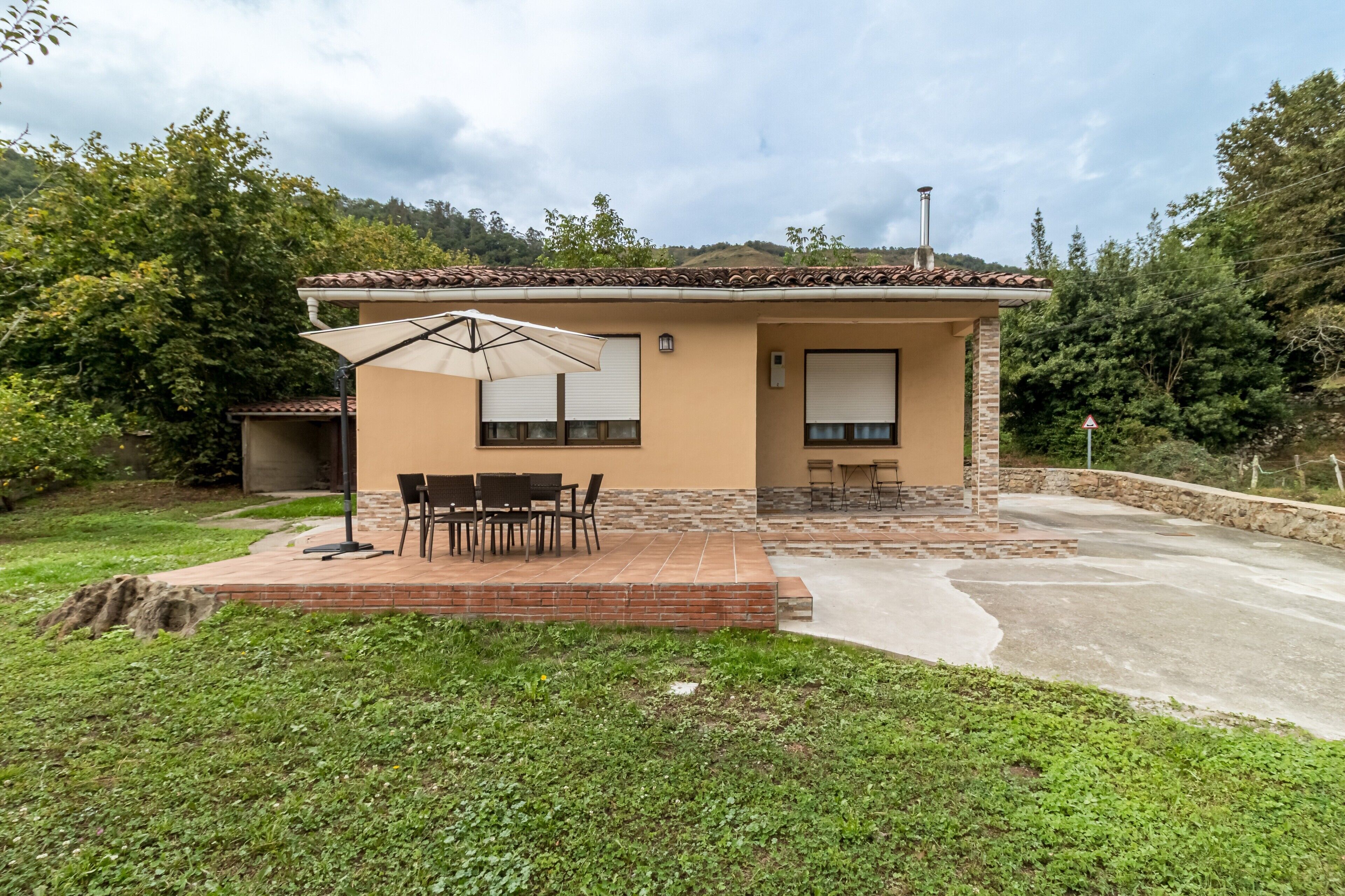 Una casa de un piso con patio, una mesa y sillas, y un área cubierta con sombrilla.