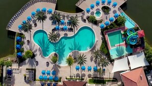 Vista aérea de un complejo turístico con una piscina central, un tobogán acuático y varias zonas de descanso con sombrillas.