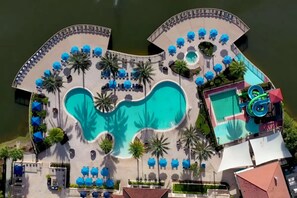 Vue aérienne d’un complexe hôtelier doté d’une piscine centrale, d’un toboggan aquatique et de plusieurs espaces de détente agrémentés de parasols.