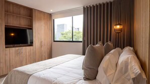 Una habitación de hotel moderna con una cama grande, un televisor de pantalla plana y un ventanal con cortinas.