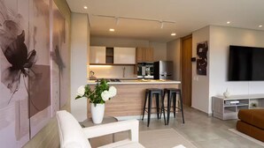 Una cocina moderna con una isla central, taburetes de bar y una zona de comedor con una silla blanca.