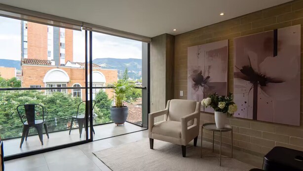 Una habitación moderna con balcón, un sillón color beige, una mesita pequeña y dos sillas.