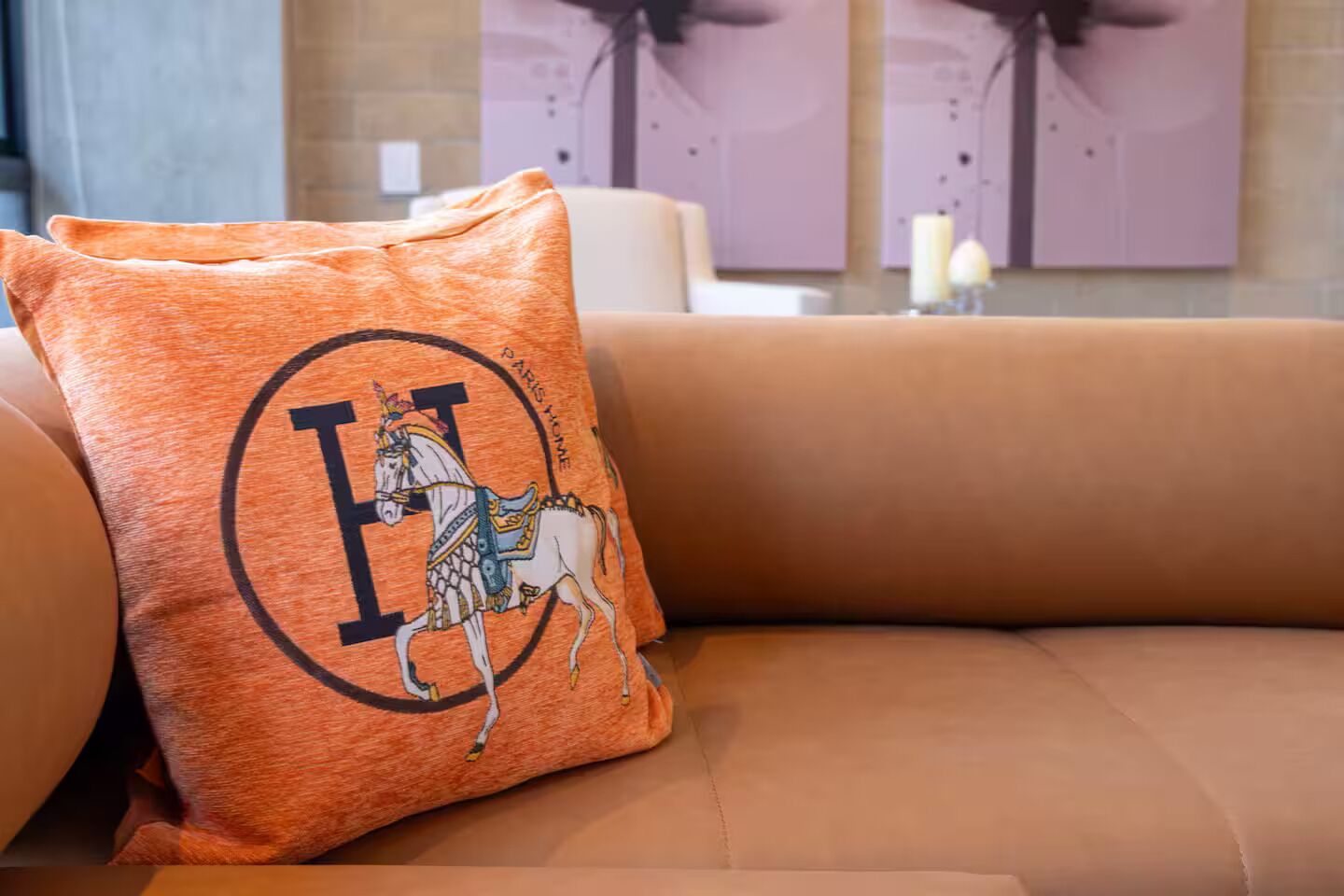 A beige sofa with a decorative orange pillow featuring a horse and rider design.
