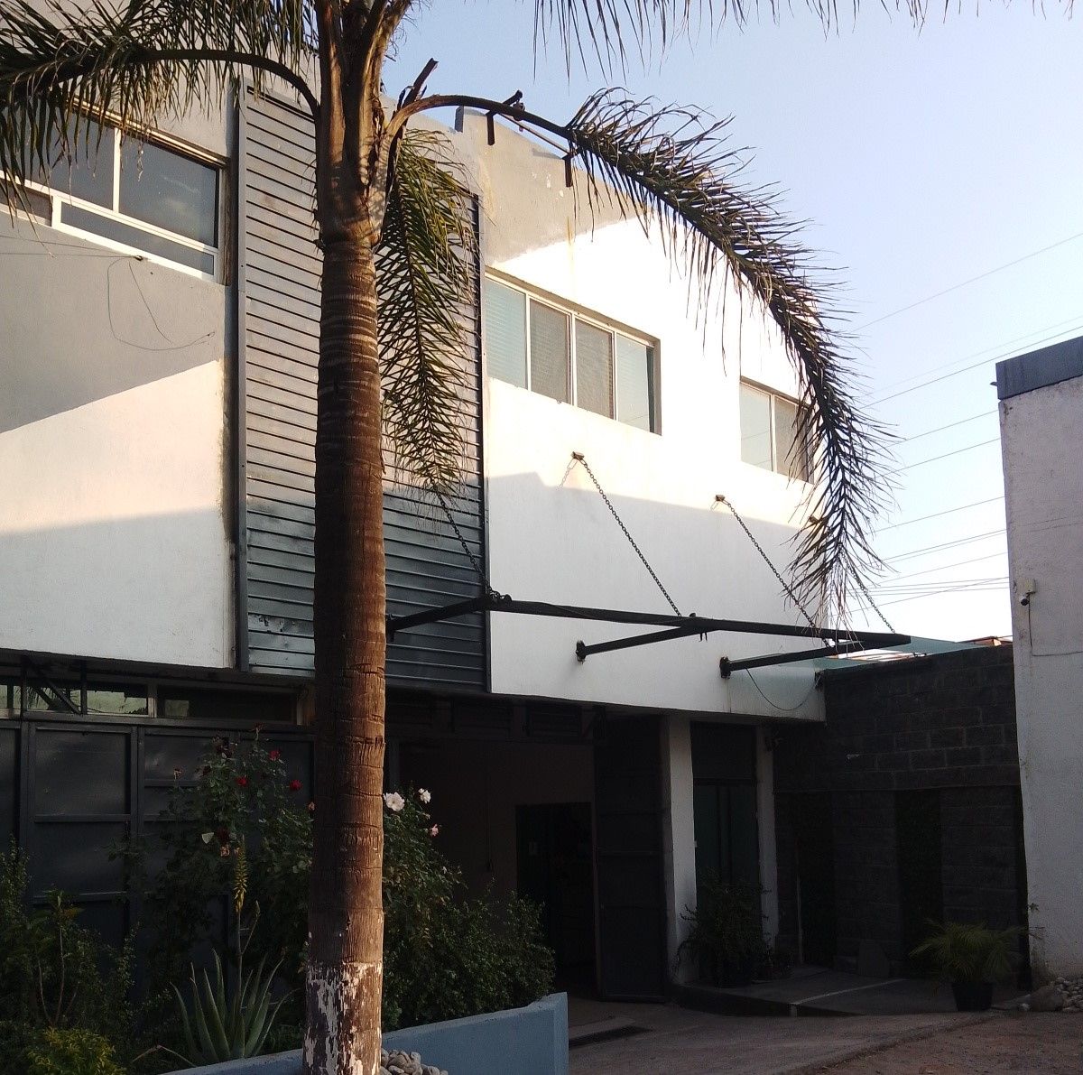 Un edificio de dos pisos con techo plano, un patio cubierto y una palmera.