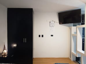 Una habitación con un armario negro, televisor montado y suelo de madera.