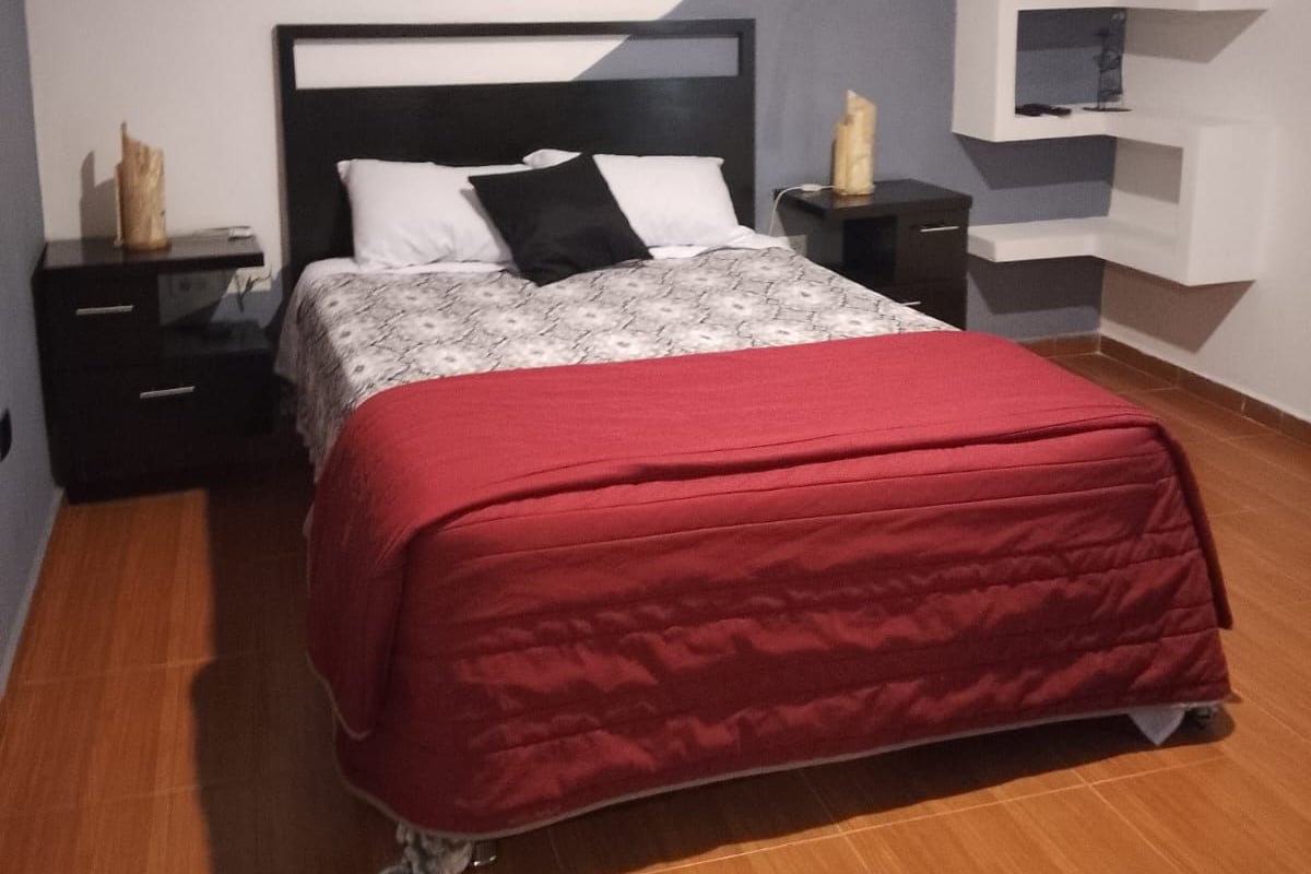 Un dormitorio con cama, mesitas de noche, un aparador, una colcha roja y una estantería empotrada.