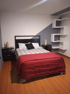 Un dormitorio con cama, mesitas de noche, un aparador, una colcha roja y una estantería empotrada.