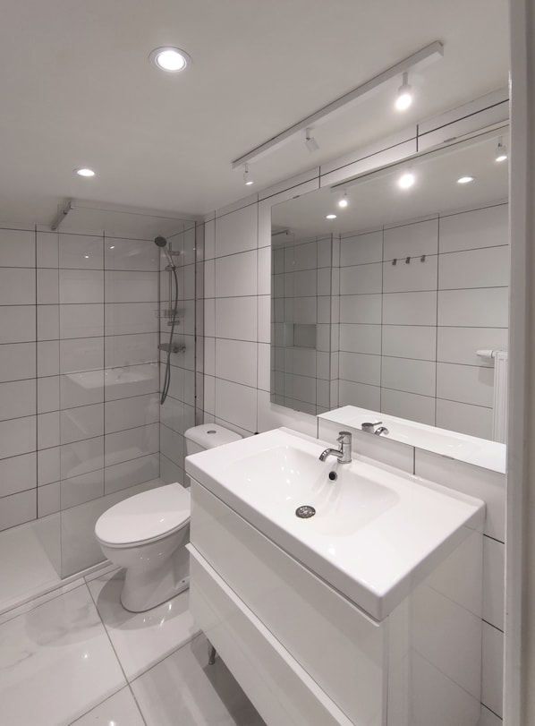 A modern bathroom with a white sink, mirror, and toilet. - me more studio (Mons)