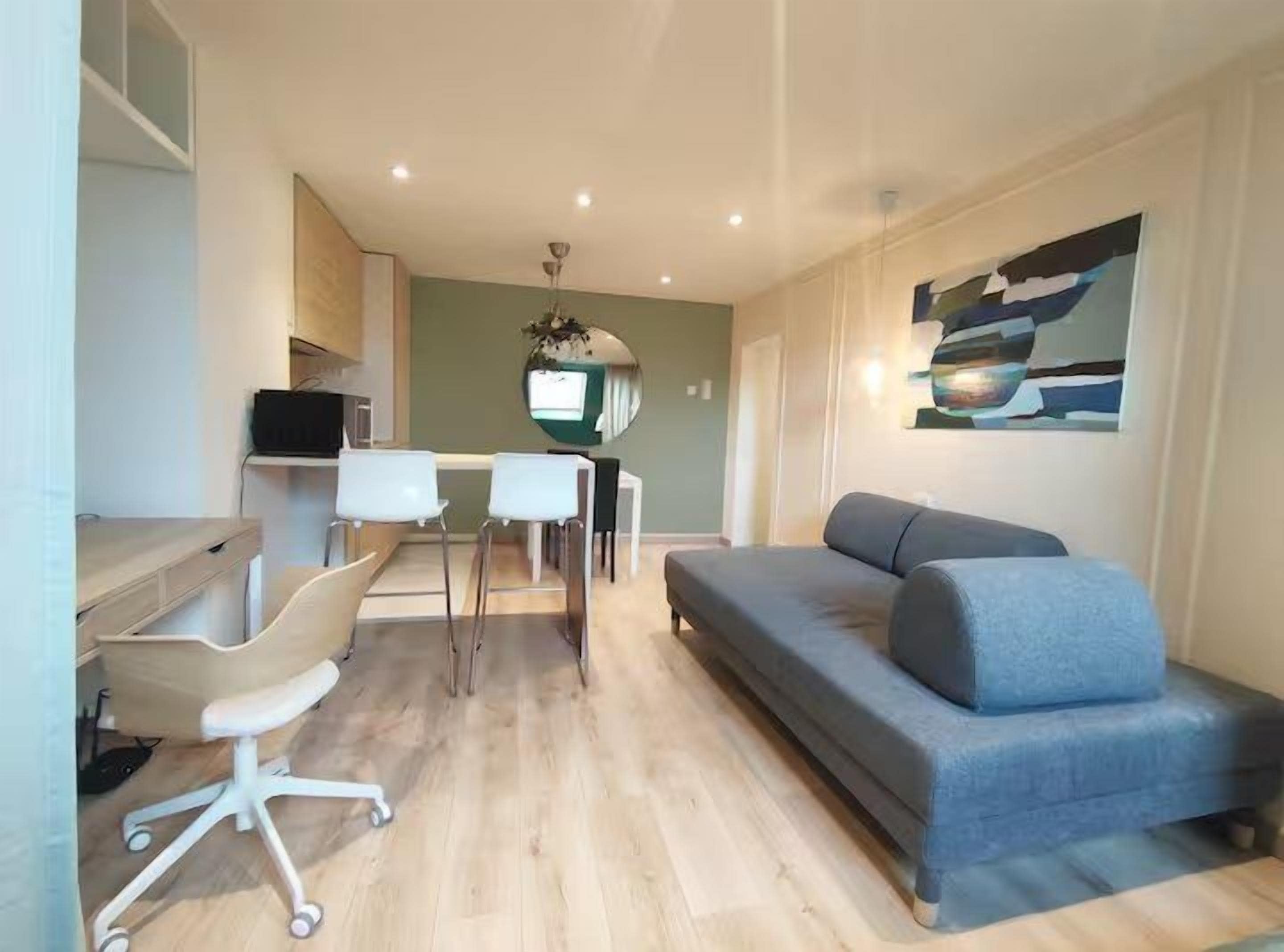 A modern living room with a sofa, a dining table with chairs, and a TV.