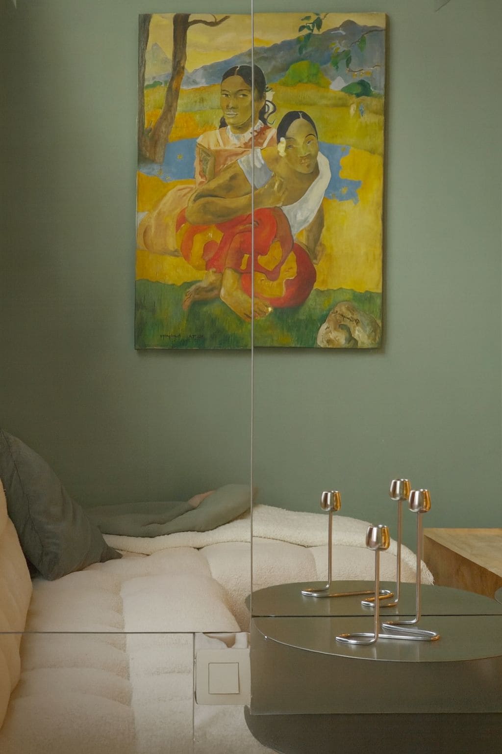 Una habitación con un cuadro en la pared, una cama con cubre cama blanco y una mesa con tres vasos.