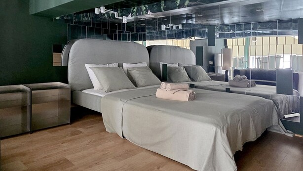 A modern bedroom with two beds, a large window, and a unique ceiling design.