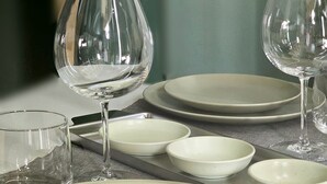 A table set with plates, bowls, and wine glasses, arranged on a textured tablecloth.