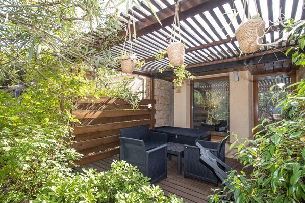 A covered patio area with wicker hanging baskets, a wooden deck, and outdoor furniture.