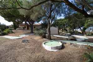 Un parcours de golf doté de plusieurs greens d’entraînement, d’arbres et d’un bâtiment visible au loin.