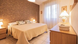 Ein Schlafzimmer mit einem Bett, Nachttischen, einer Kommode, einer Lampe und einem Fenster mit Vorhängen.