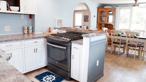 A kitchen with white cabinets, a black stove, and a blue rug with a white design. - Eazy Breezy Beach Home (Dennis)