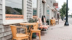 Outdoor seating with wooden chairs and tables, a brick sidewalk, and storefronts with signs. - Eazy Breezy Beach Home (Dennis)