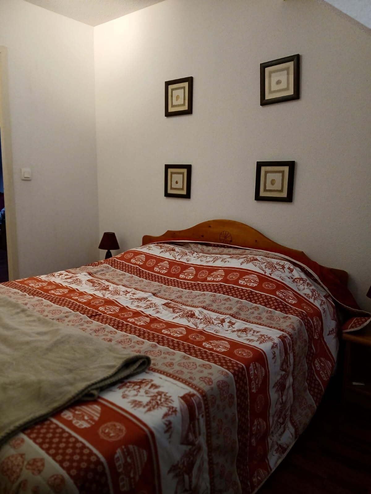 A bedroom with a bed, a nightstand, and a lamp. There are four framed pictures on the wall.