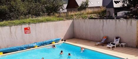 Una piscina con gente, rodeada por un muro de hormigón y con una montaña al fondo.