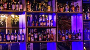 Uma área de bar com prateleiras cheias de garrafas de bebidas e um laptop sobre uma mesa de madeira.