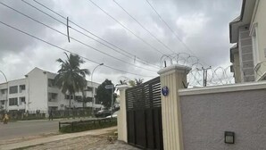 Uma entrada com portão, placa de número, um caminho de acesso pavimentado e um edifício ao fundo.